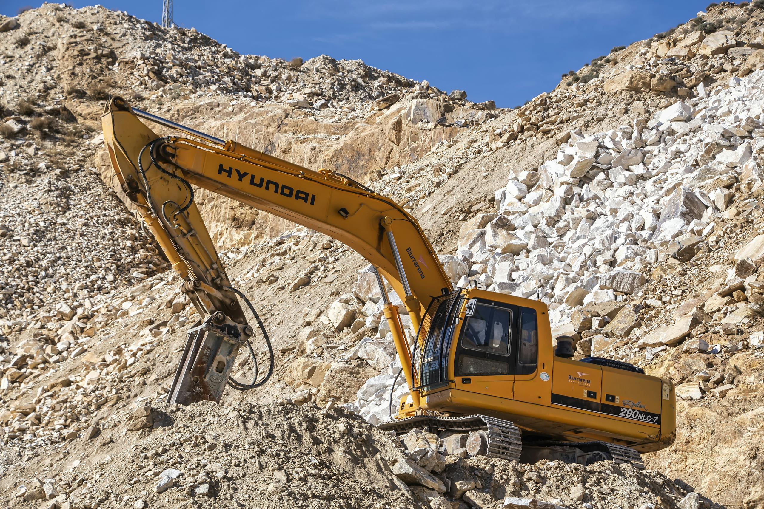 Yellow Hyundai excavator operating in a rocky quarry under a clear blue sky. Perfect for industrial themes.